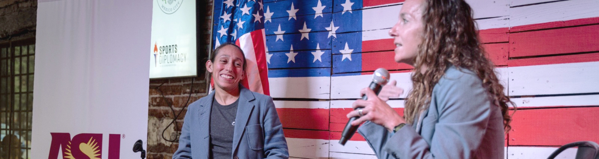 Woman on stage speaking at event with attendee in background